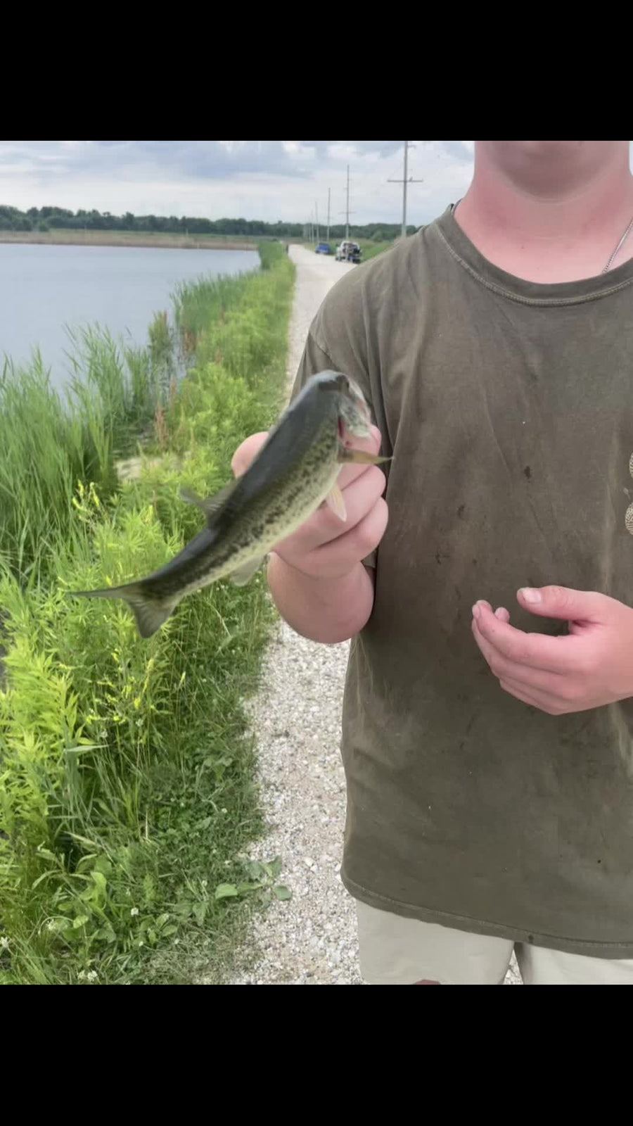 Angler holding a bass on a gravel bank